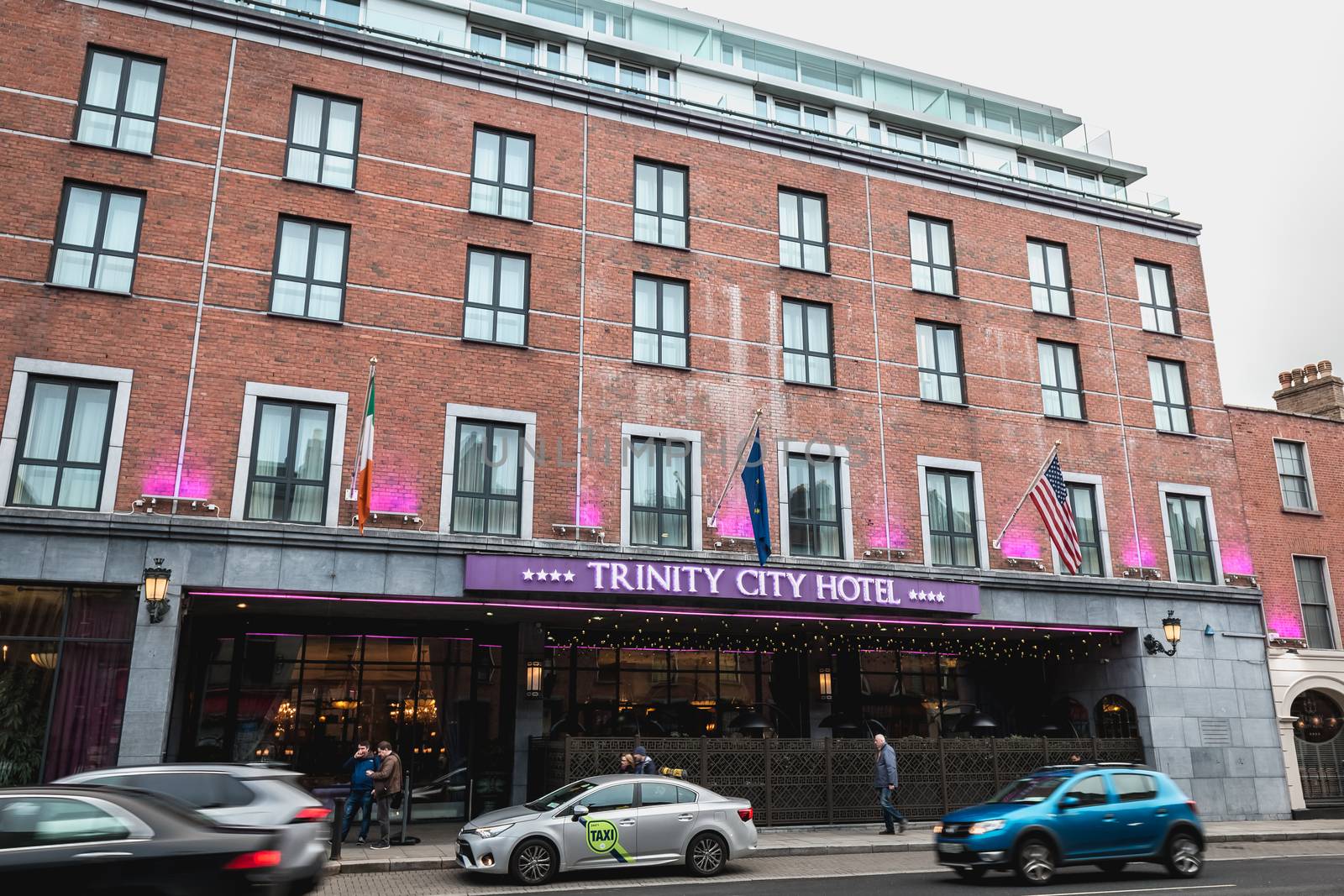 People and cars driving past the facade of the luxurious Trinity by AtlanticEUROSTOXX