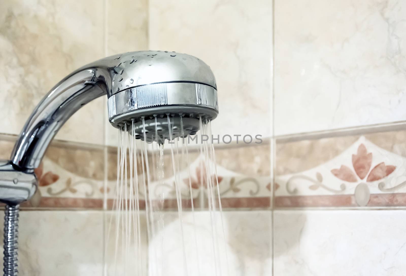 Interior of a shower with water flowing from the shower head. Droplets and moisture. Walls with decorated tiles. Hygiene and personal care