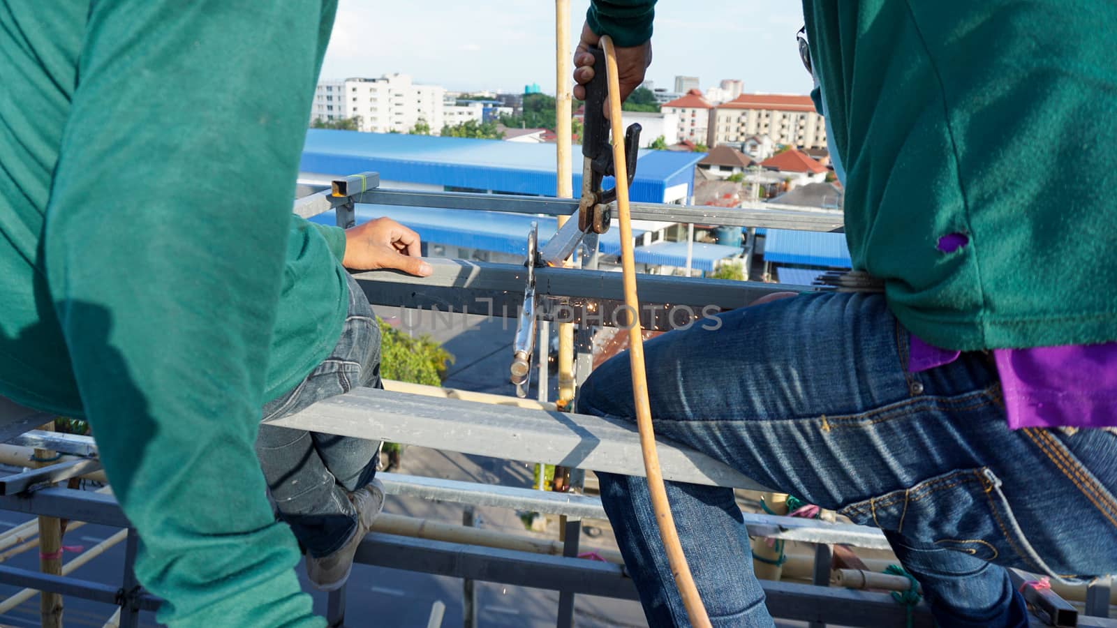 Welding of metal structures with soldering steel beam structure on extension of a building on construction site. Sparks and smoke fly as steel is welded.