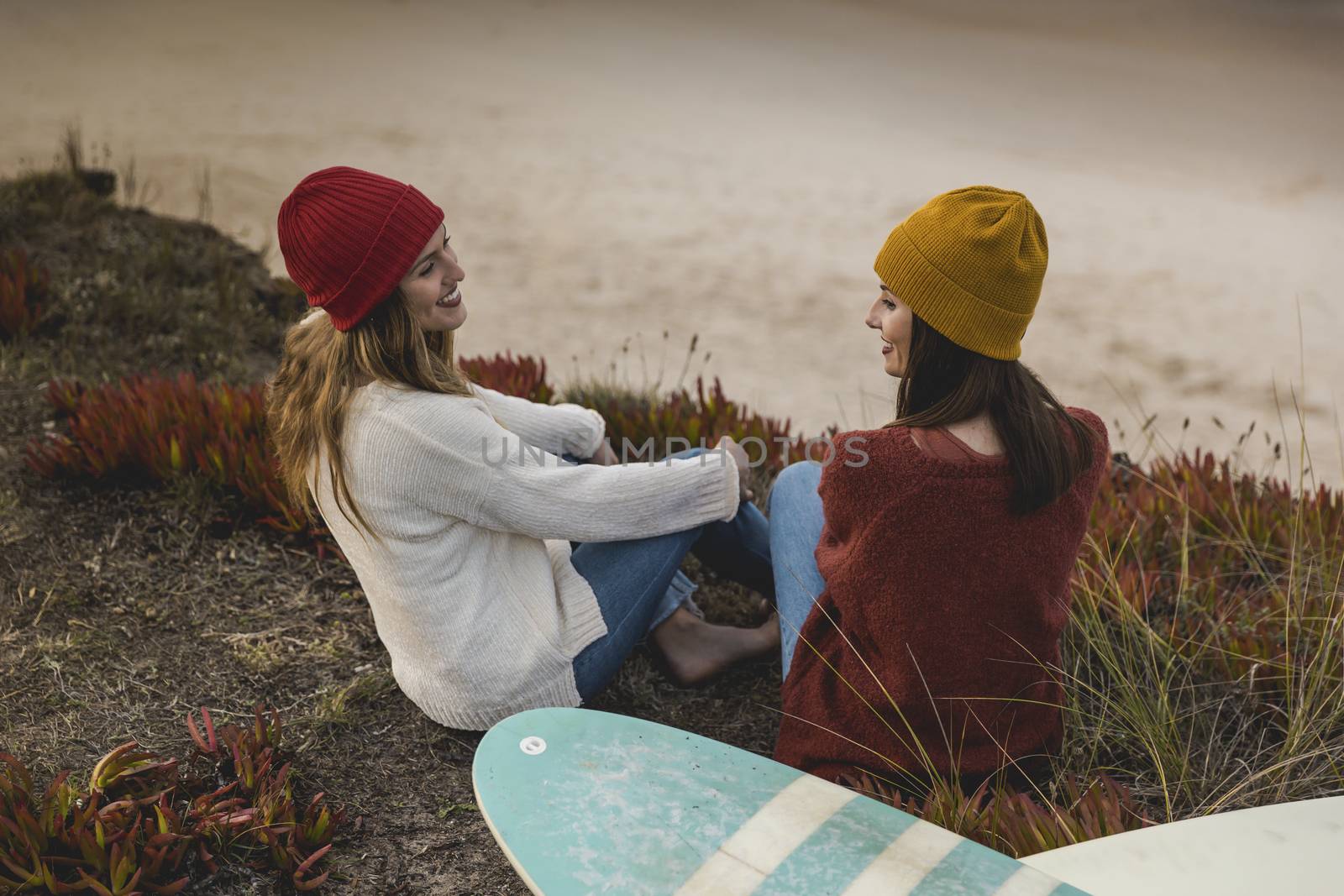 Two best friends sitting near the coastline with her surfboards while looking to the ocean