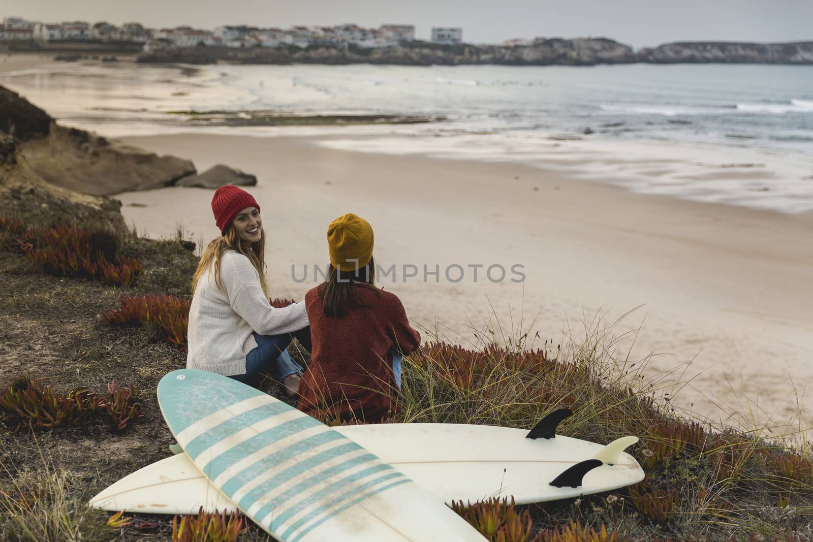 Two best friends sitting near the coastline with her surfboards while looking to the ocean