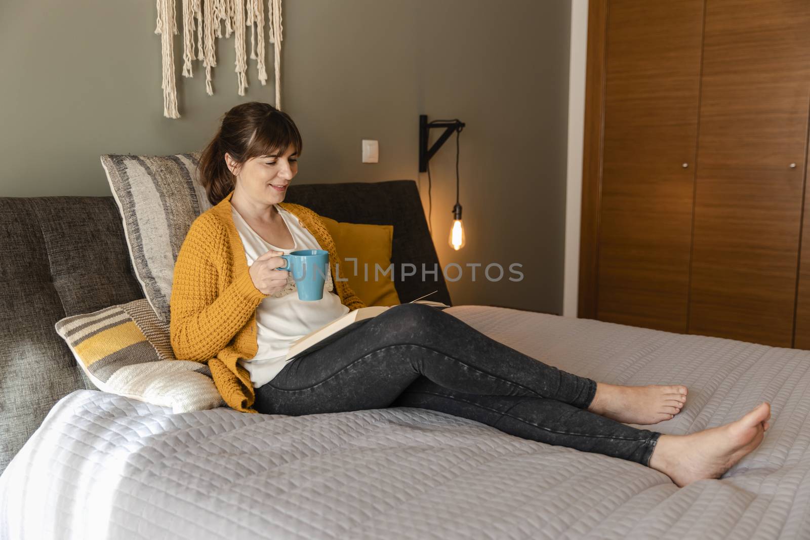 Beautiful woman on bed with a cup of coffee and reading a book