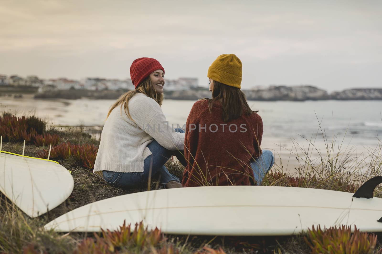 Two best friends sitting near the coastline with her surfboards while looking to the ocean