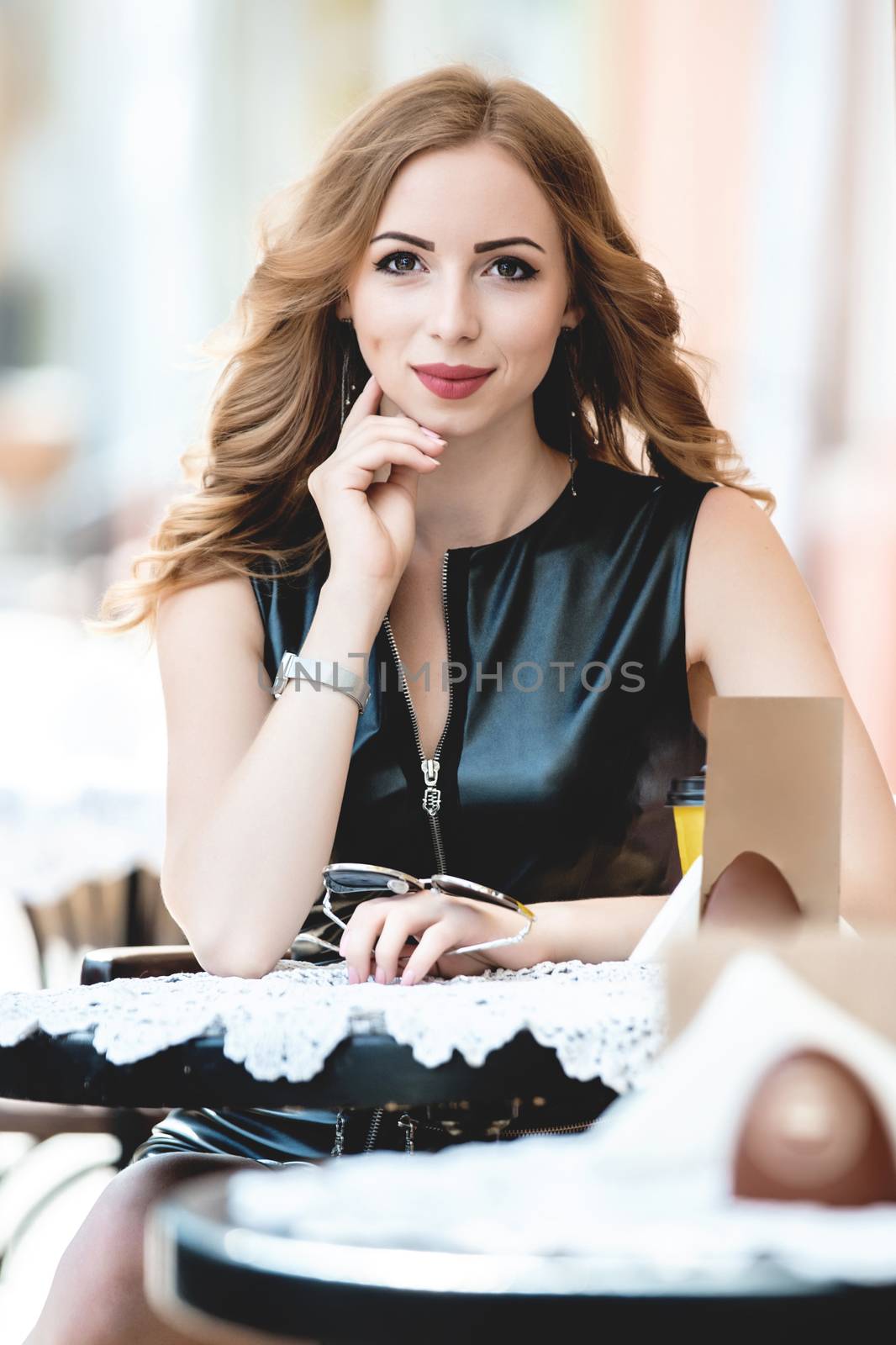 Attractive young caucasian woman sitting in street cafe, waiting for someone, having coffee, having great time. She wearing black stylish dress,