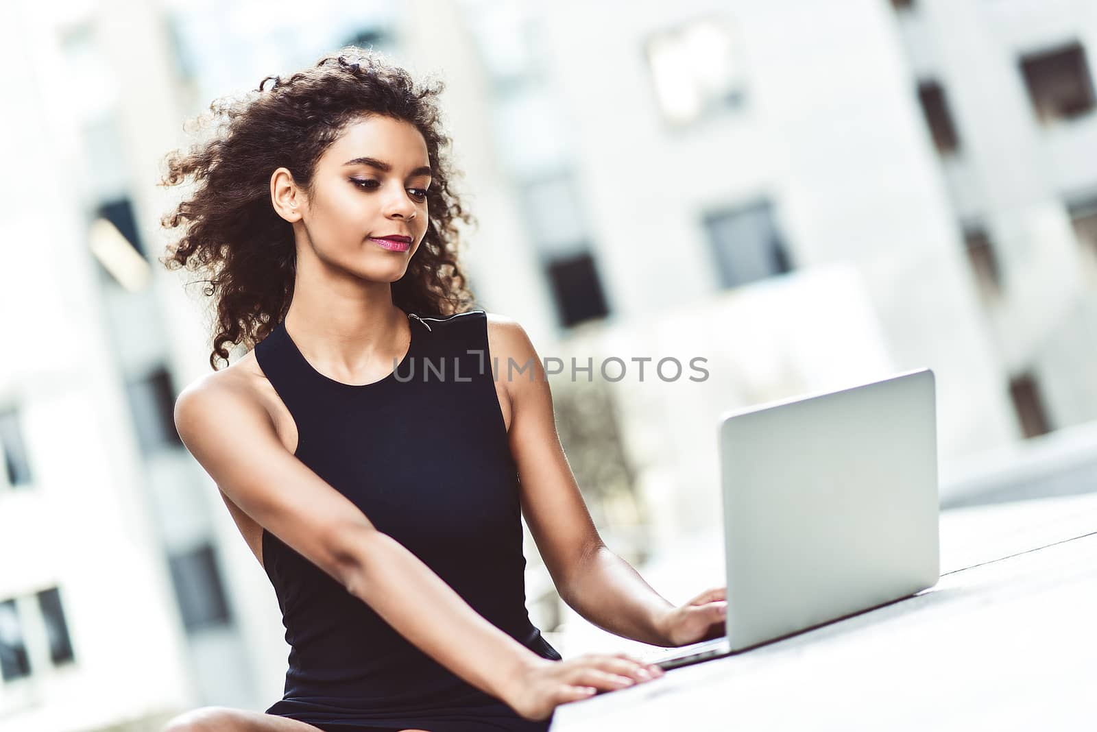 Young attractive mixed race girl with beautiful afro hair who is smiling looking at her laptop screen during video call. Young woman using laptop.
