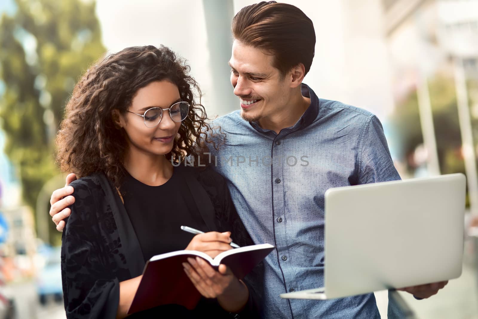 Business man and woman working on laptop together on building background in city outdoor feeling happy.