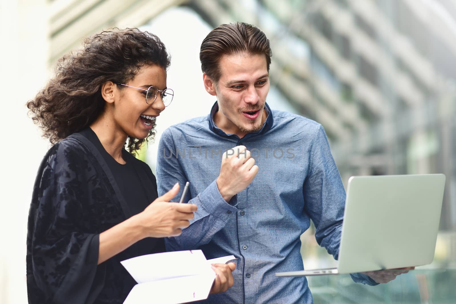 Business man and woman working on laptop together on building background in city outdoor feeling happy.