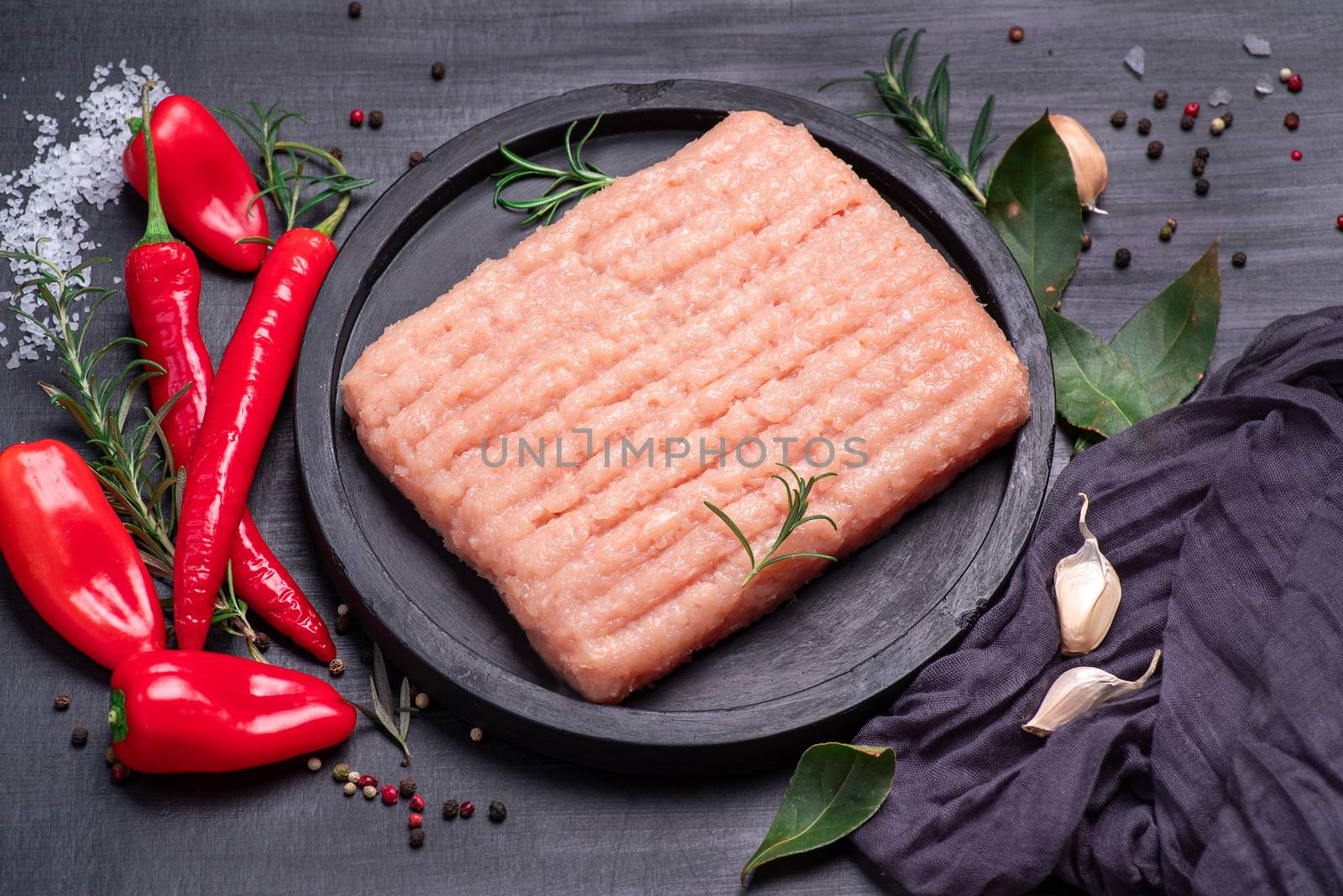 Raw minced chicken on a black plate on a wooden table. Top view. Minced chicken close-up. Delicious diet meat.Raw Minced meat with herbs and spices by nkooume