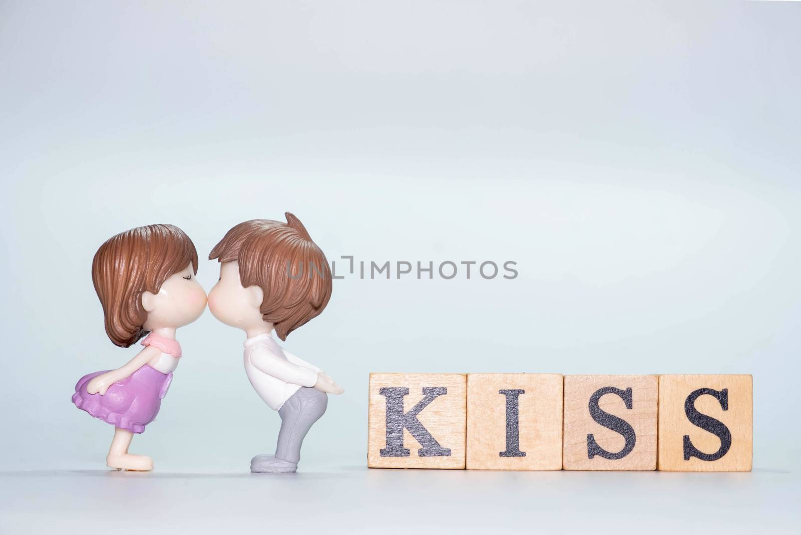 The Miniature doll of couple boy and girl kiss and have Wooden alphabet word KISS isolate on White background