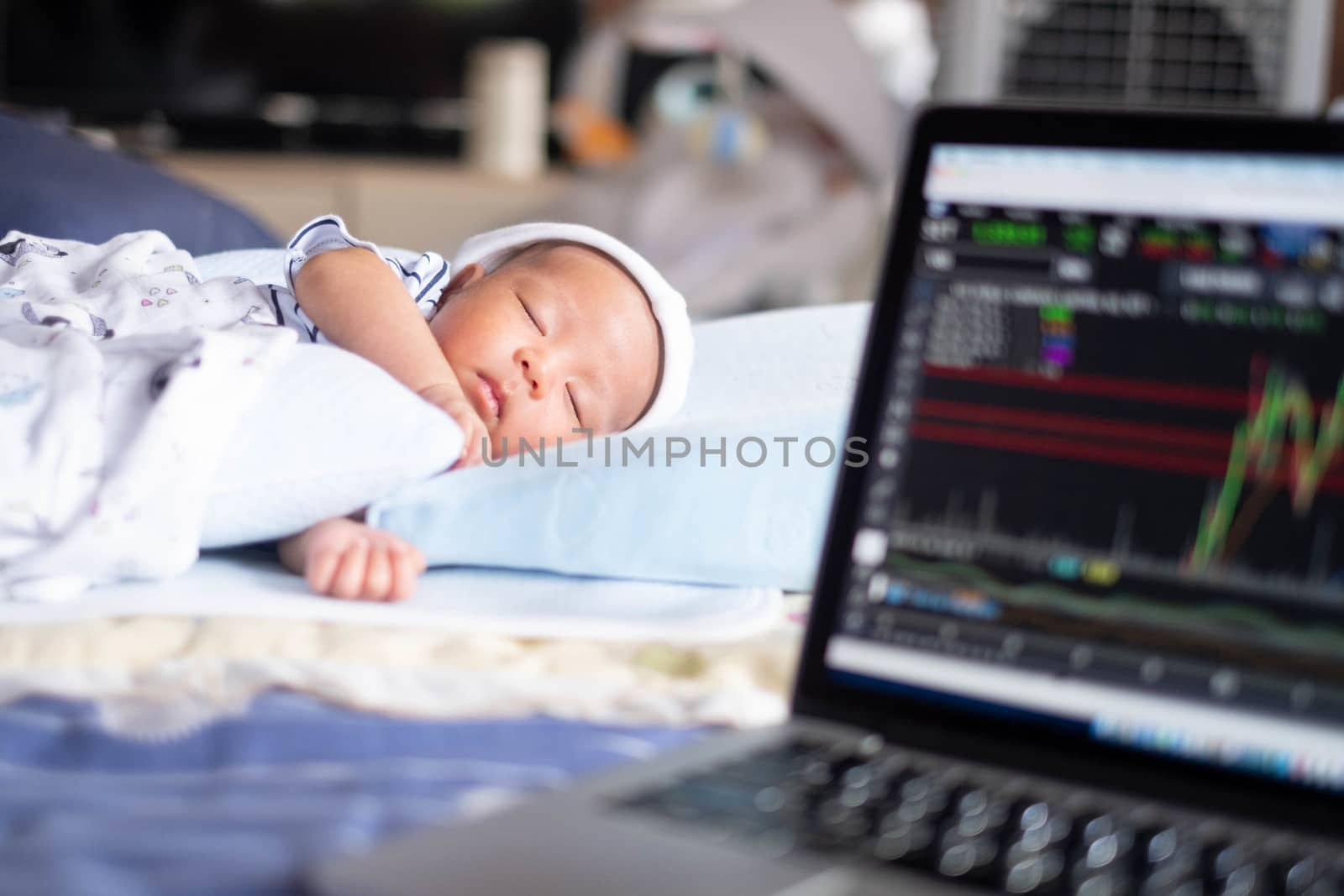 Soft focus on baby .The parents father Stock trader trading stock on his laptop while his newborn infant baby sleep on the bed