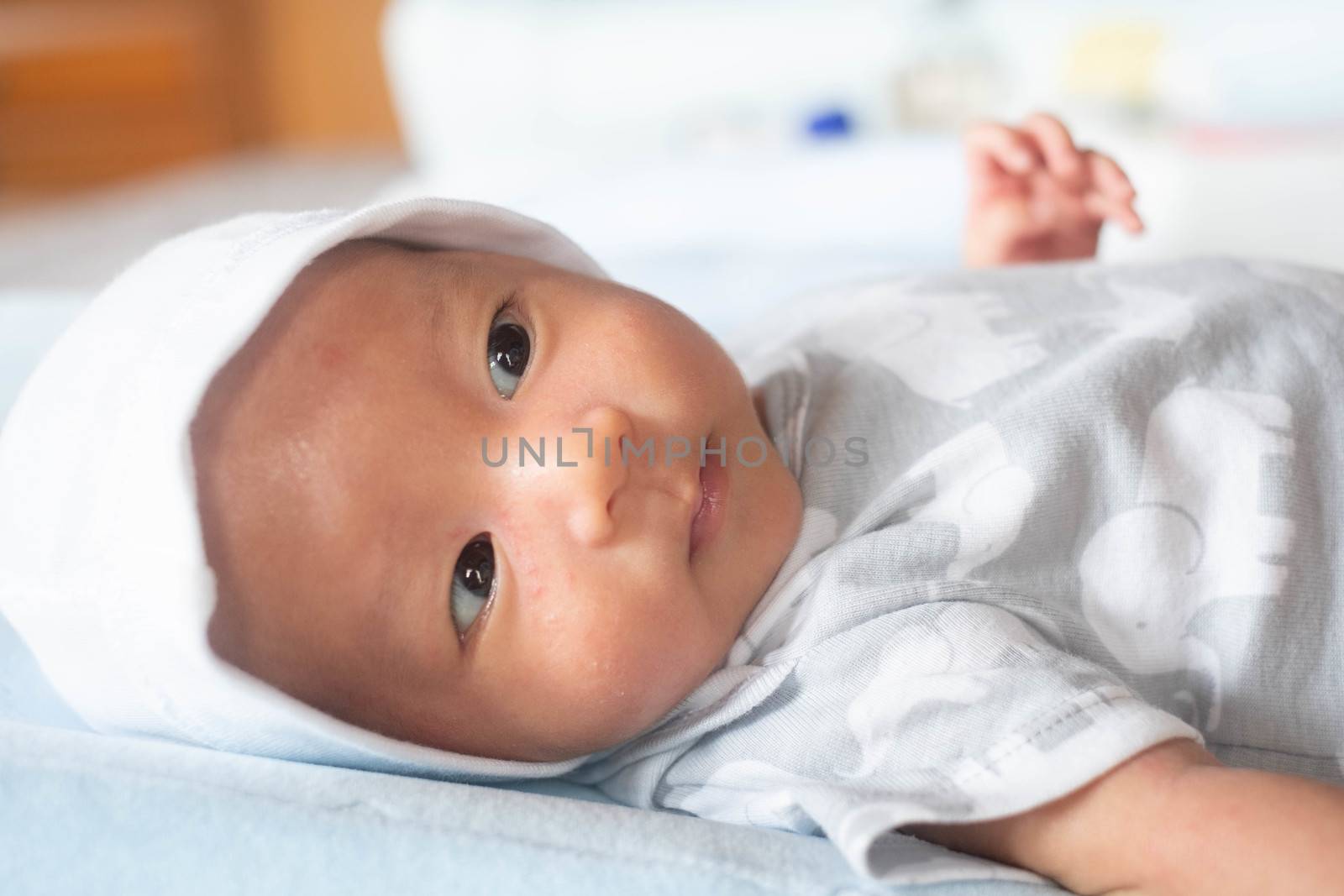 Portrait Photo of happy newborn baby infant with big black eyes lay down on the bed