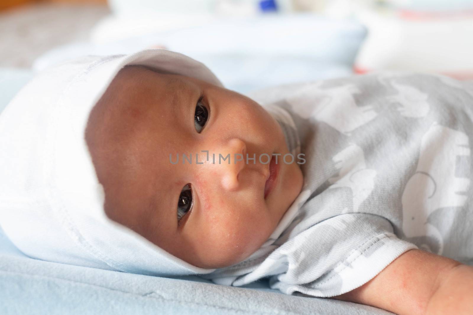 Portrait Photo of happy newborn baby infant with big black eyes lay down on the bed