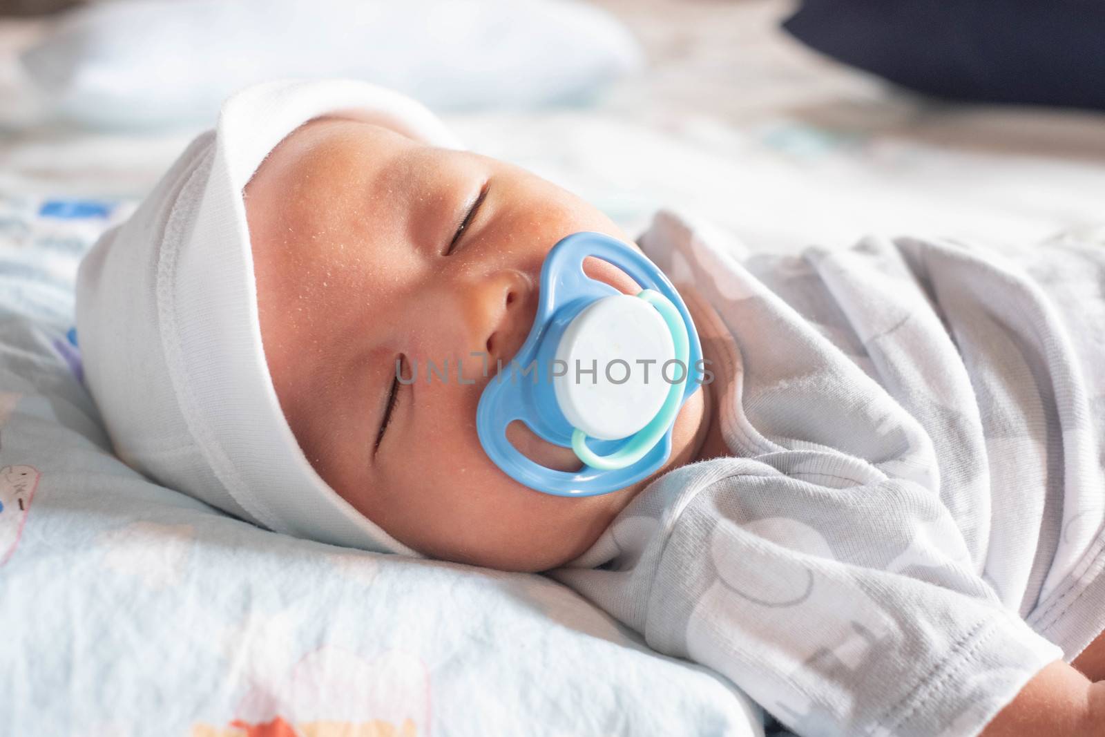 Infant newborn baby boy sleeping peacefully with pacifier on the bed