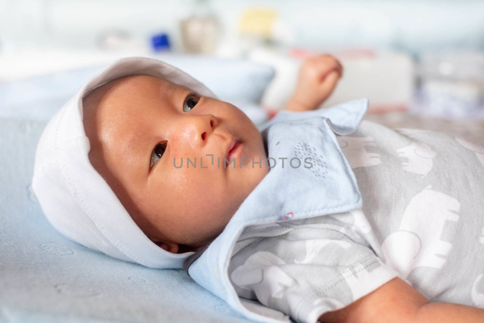 Portrait Photo of happy newborn baby infant with big black eyes lay down on the bed