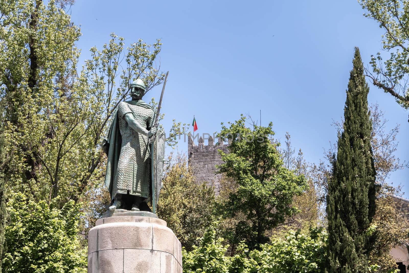 Guimaraes, Portugal - May 10, 2018: statue of the first king of Portugal, D. Afonso Henriques by the sculptor Antonio Soares dos Reis in front of the castle of Guimaraes that tourists are visiting on a spring day