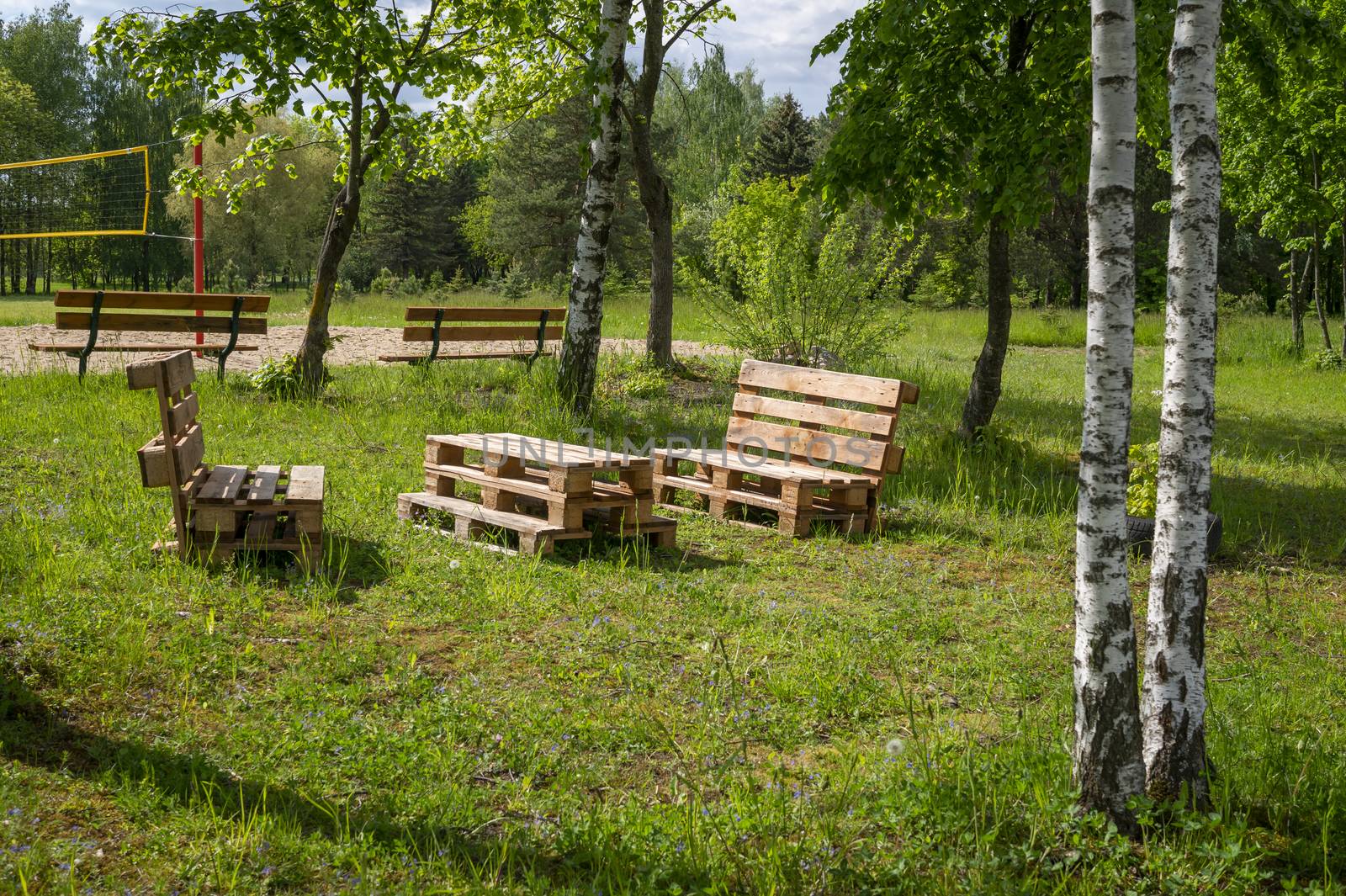 Rustic wooden table and benches made with pallets on the shore of a tranquil a lake surrounded by trees and greenery in summer sunshine