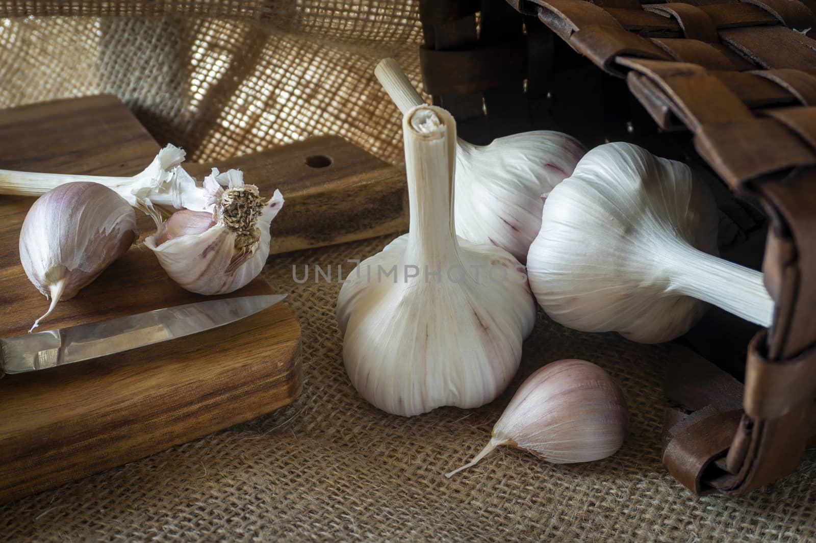Garlic bulbs and cloves in close-up on sack cloth with kitchen knife and wooden cutting board
