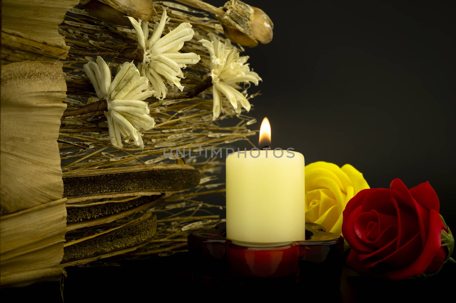 Burning yellow candle flame among flowers on a dark background