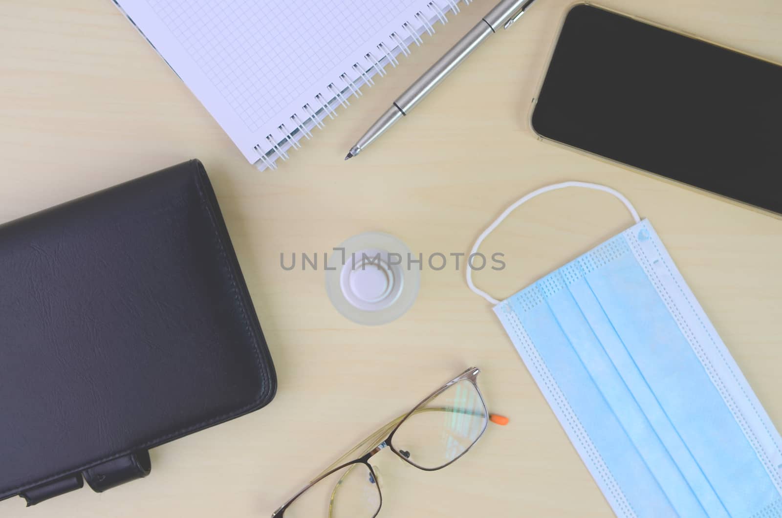 Office desk table with  face mask and sanitizer bottle or alcohol gel with smartphone isolated on wooden background, work from home and covid-19 concept and new normal.