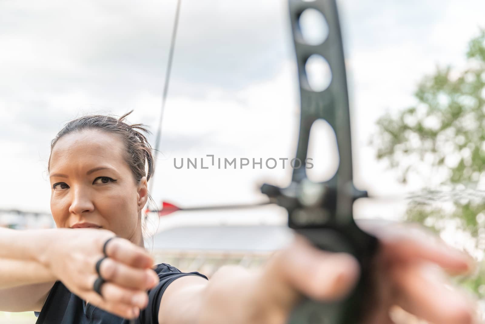 attractive spot woman stretching a bow string with an arrow on archery by Edophoto