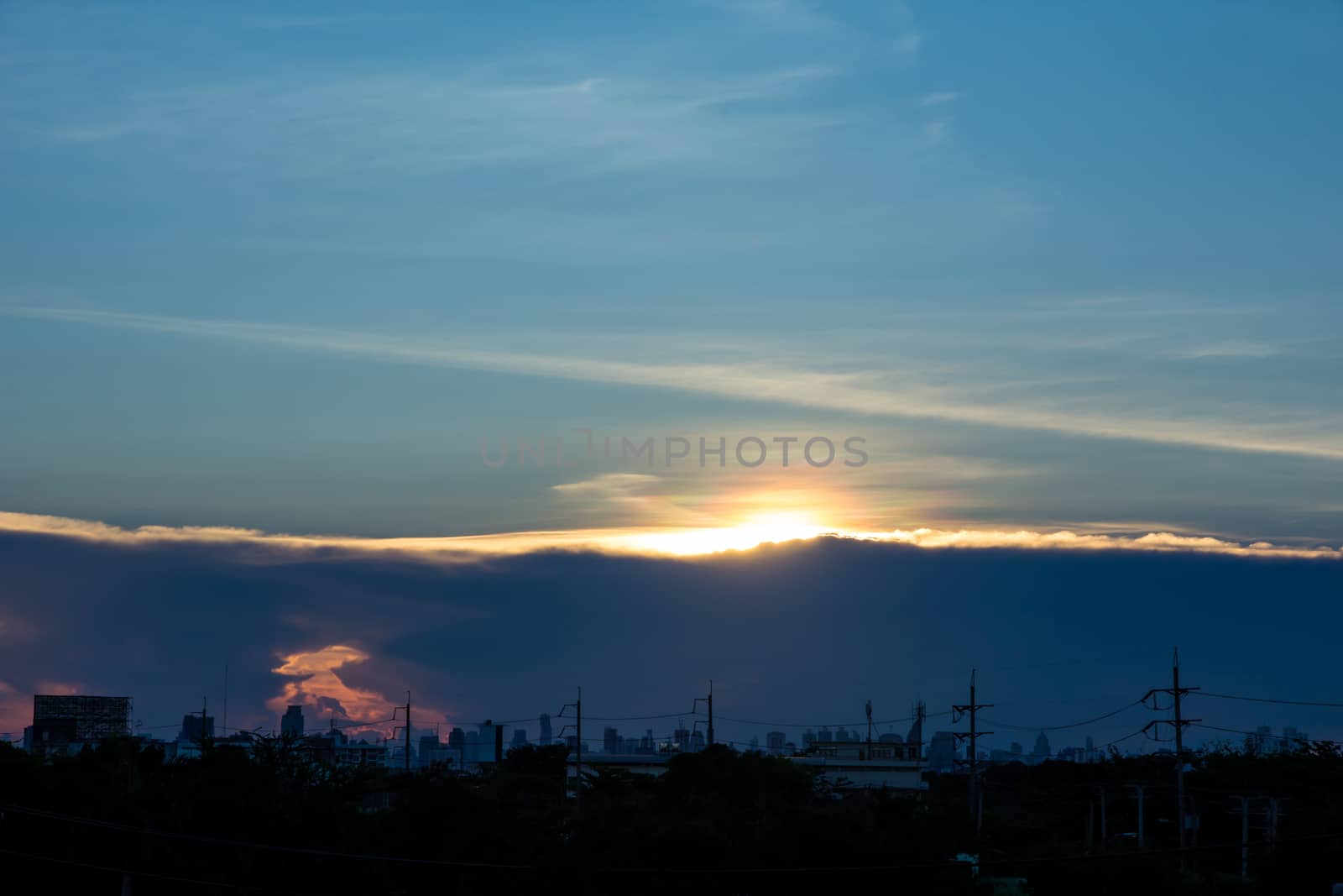 A sunset image with a cloud divides the line between the center of the image with the background as the building in the city.