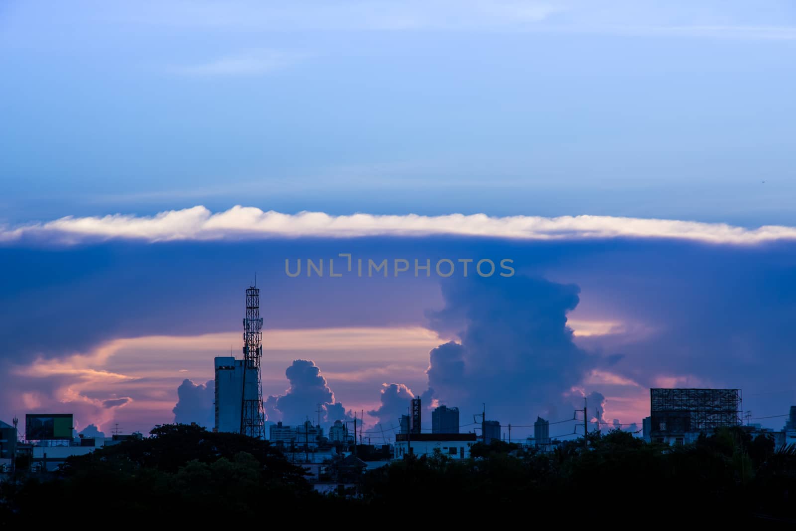 A sunset image with a cloud divides the line between the center of the image with the background as the building in the city.