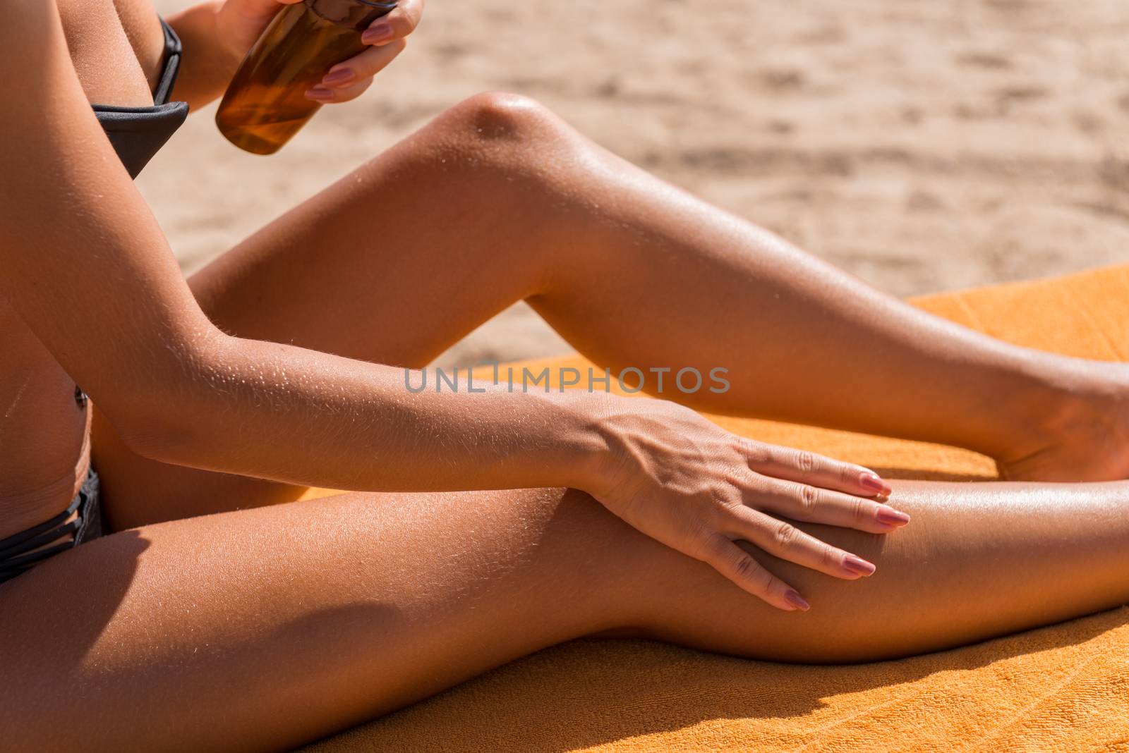 Sensuous slim woman applying suntan lotion oil to her body at the beach