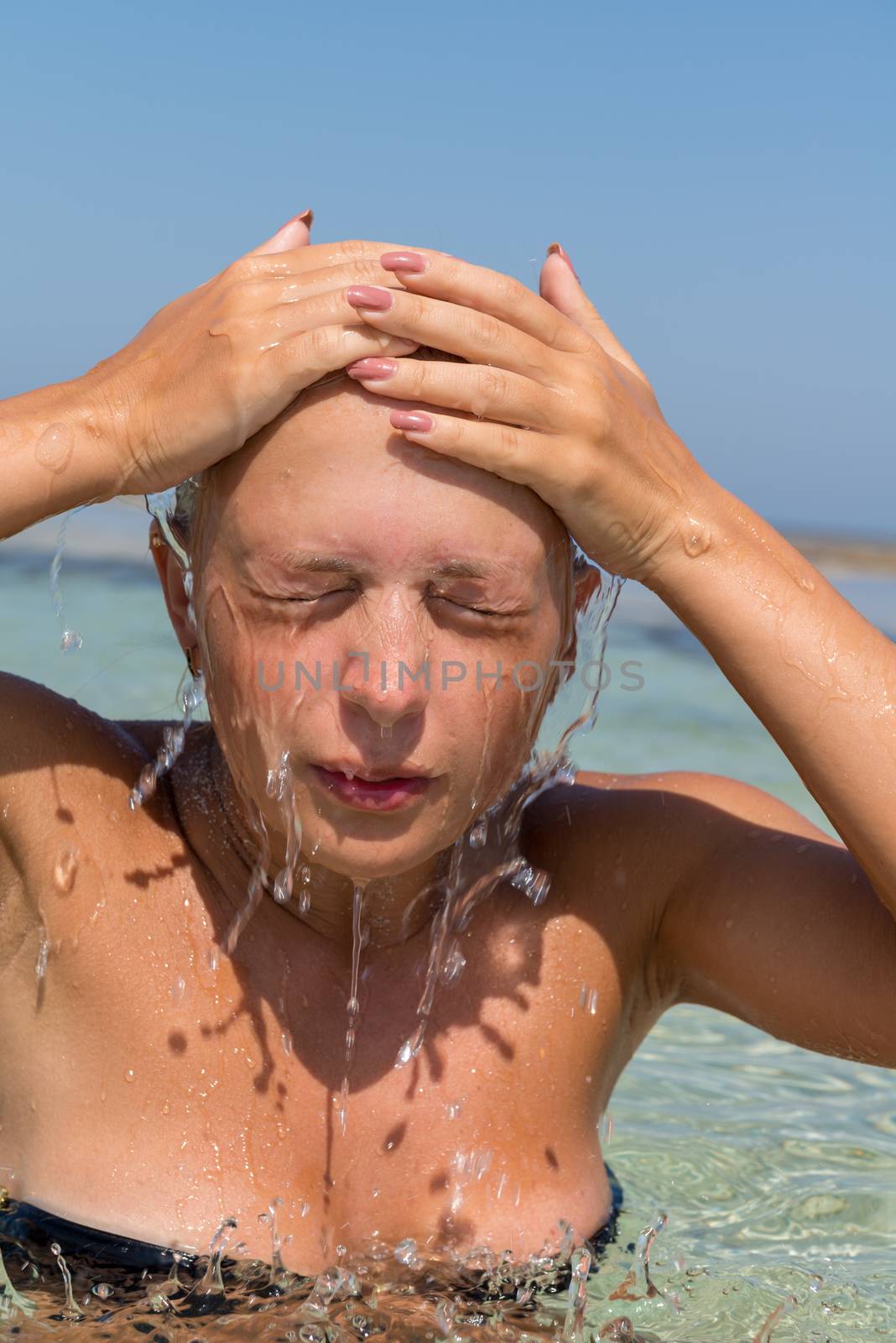 Young woman washing her face in the sea