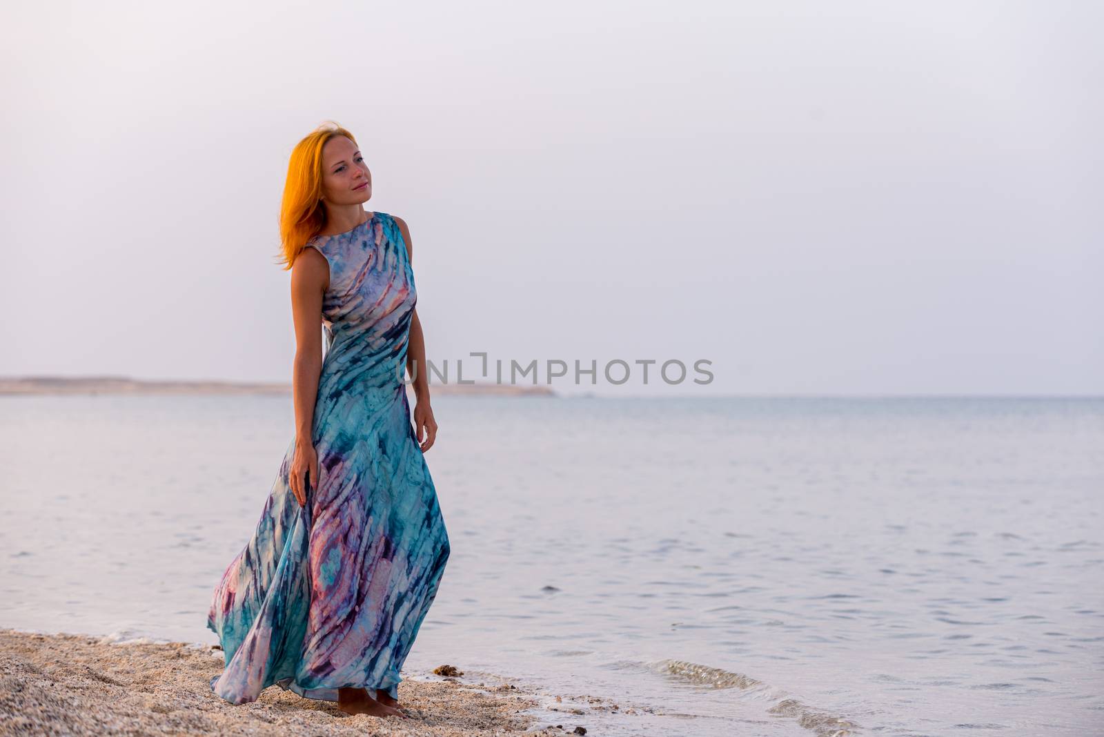 Young red woman wearing long dress on a beach