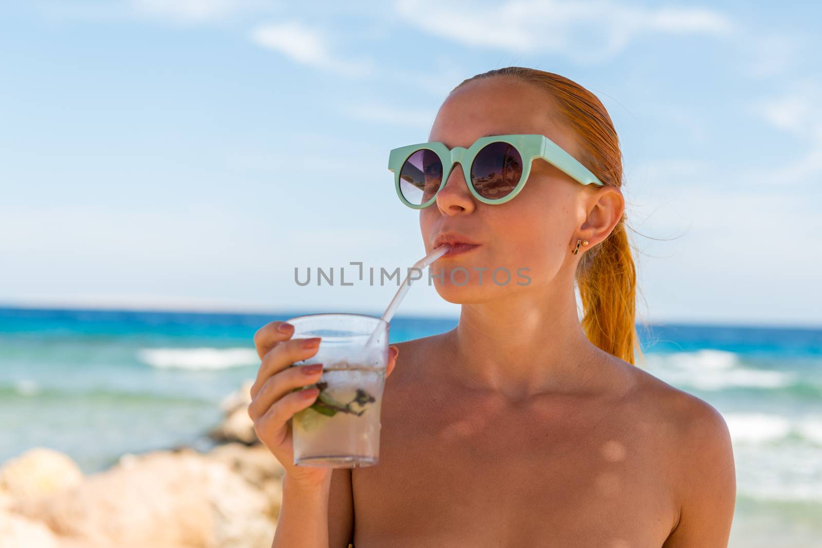 Young woman with glass of mojito wearing bikini at the beach