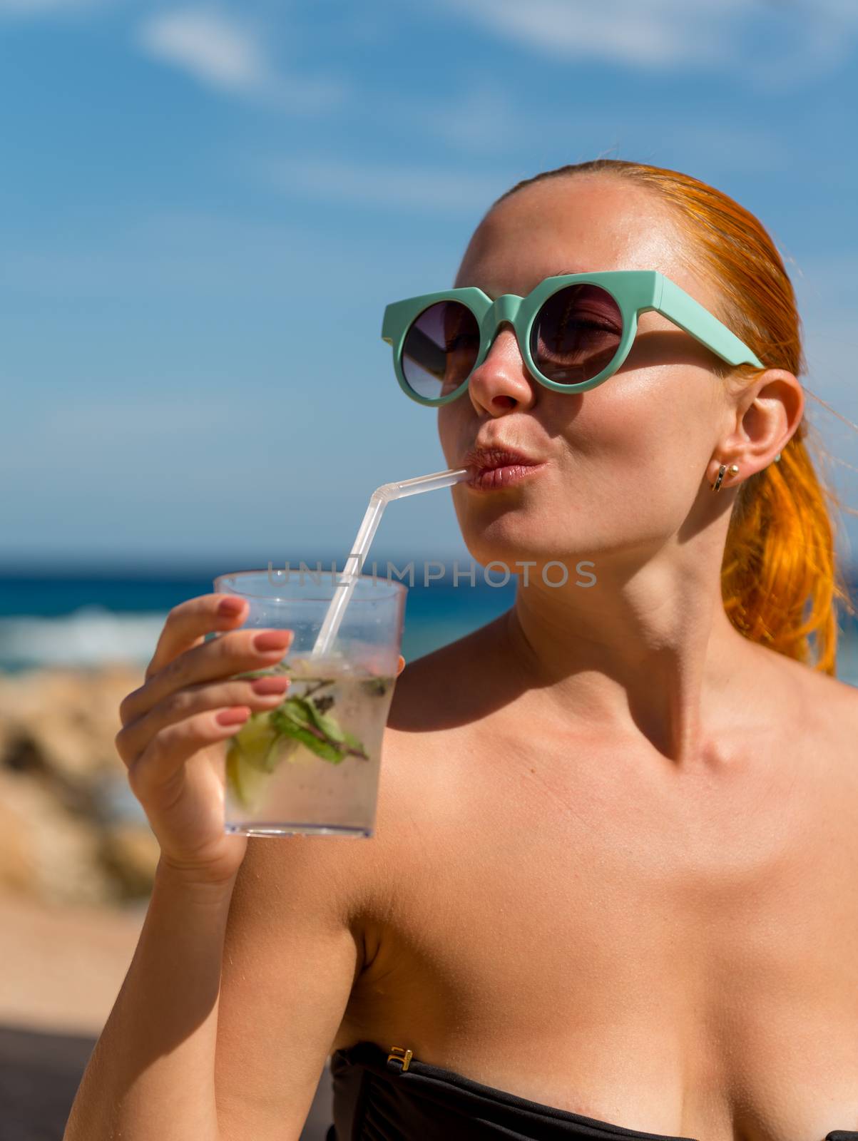 Young woman with glass of mojito wearing bikini at the beach