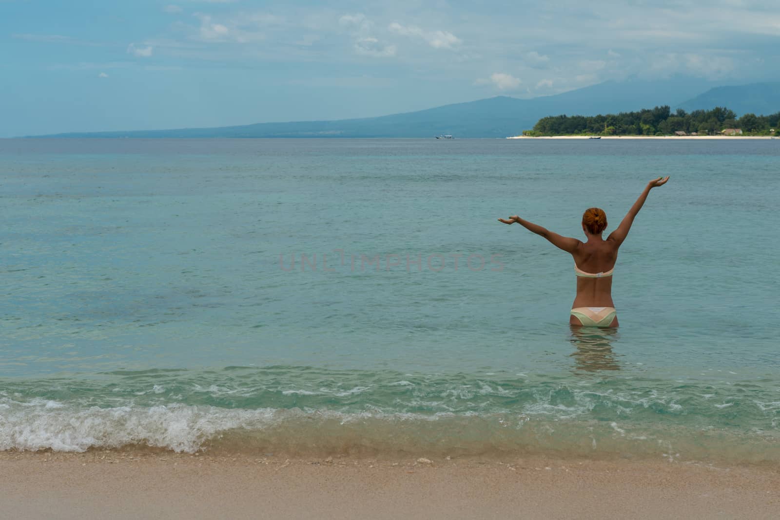 Young Woman stands in water with raised hands. Enjoying her time at tropical island beach