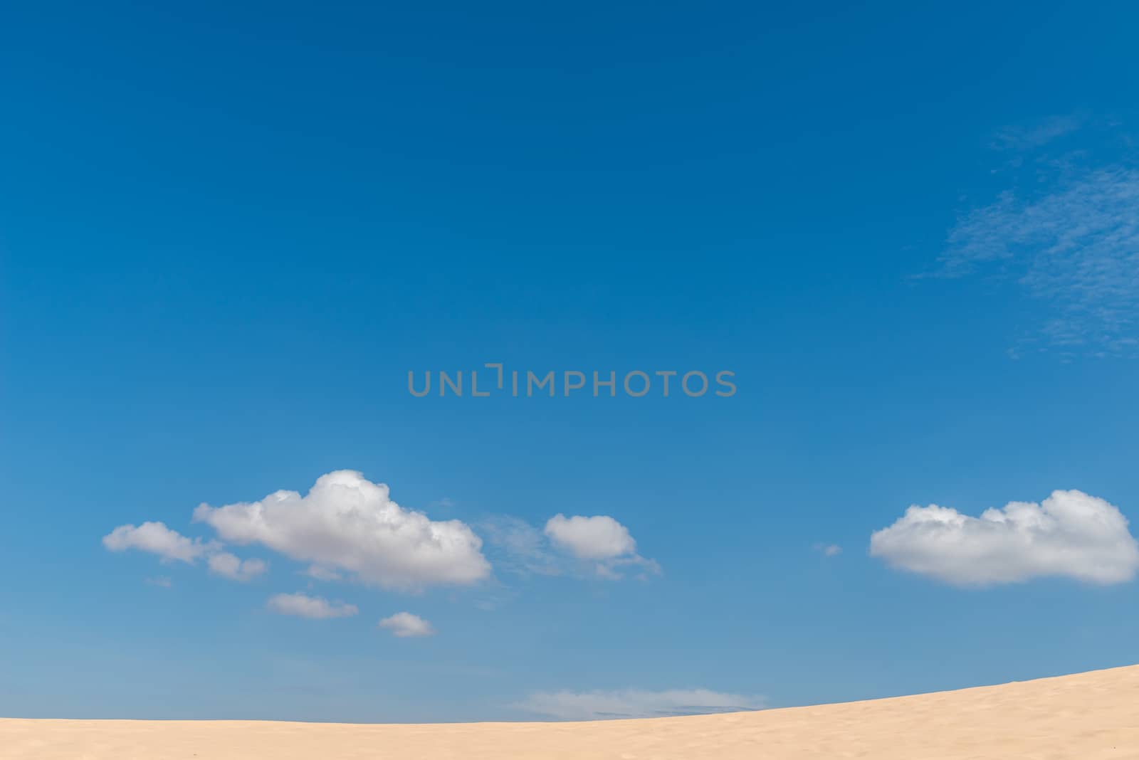 Desert sand dunes landscape with deep blue sky and clouds