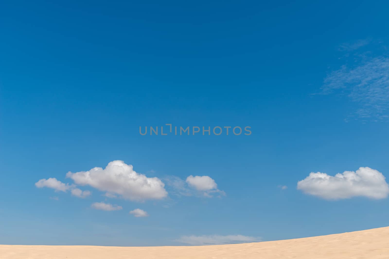 Desert sand dunes landscape with deep blue sky and clouds