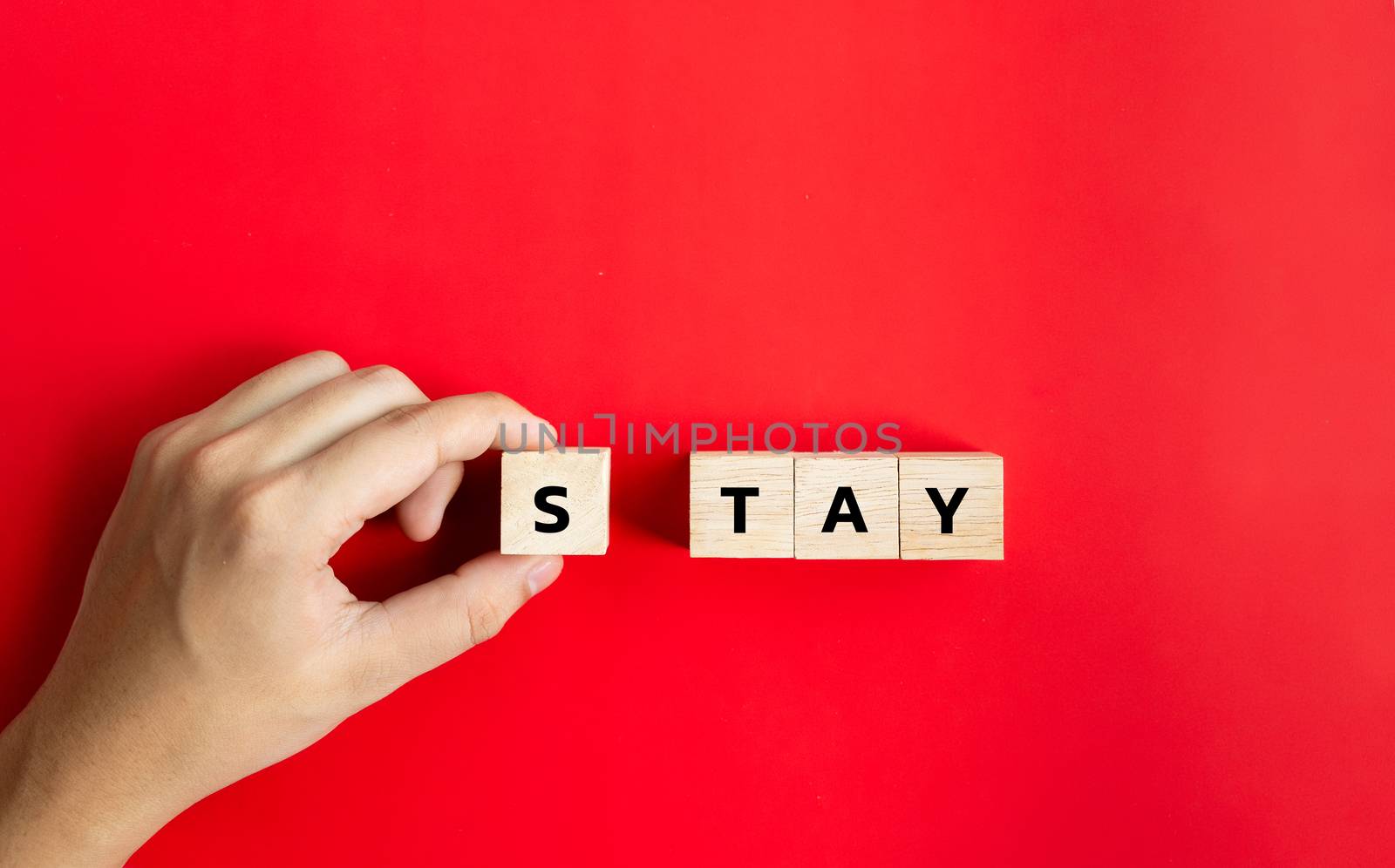 Hand hold on to the wood cube and text the word "Stay" In the concept, stay at home to stop the spread. During the corona virus outbreak or COVID-19 on red background