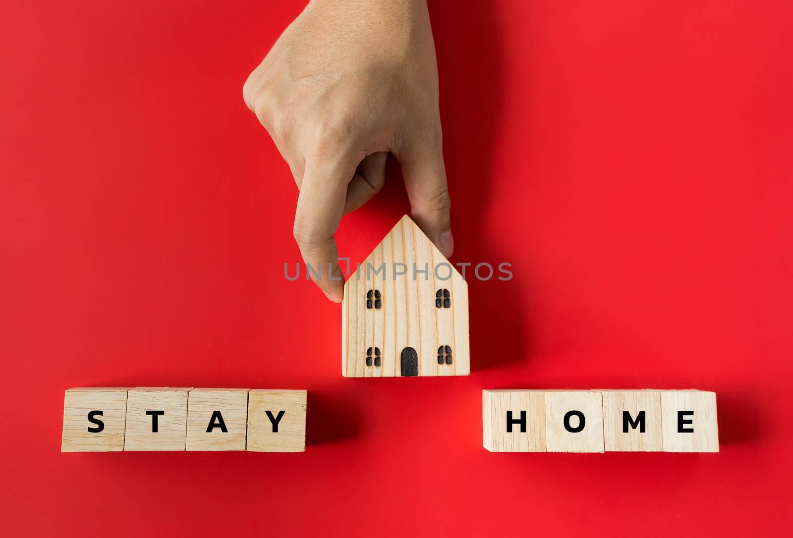 Hand hold on to the house model and text the word "Stay" on the wooden dice. In the concept, stay at home to stop the spread. During the corona virus outbreak or COVID-19 on red background