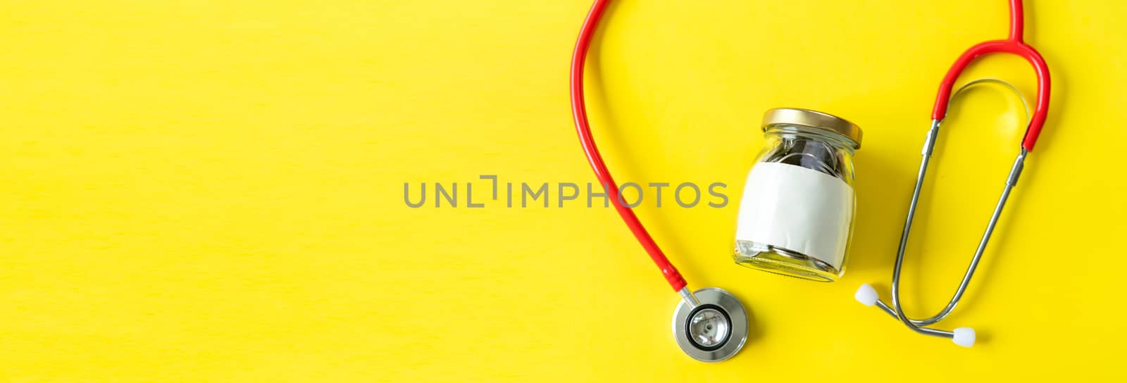 Banner of Savings and insurance concepts. Coins in a bottle with doctor headphones or red stethoscope. Saving for life insurance,retirement,health on the yellow background copy space