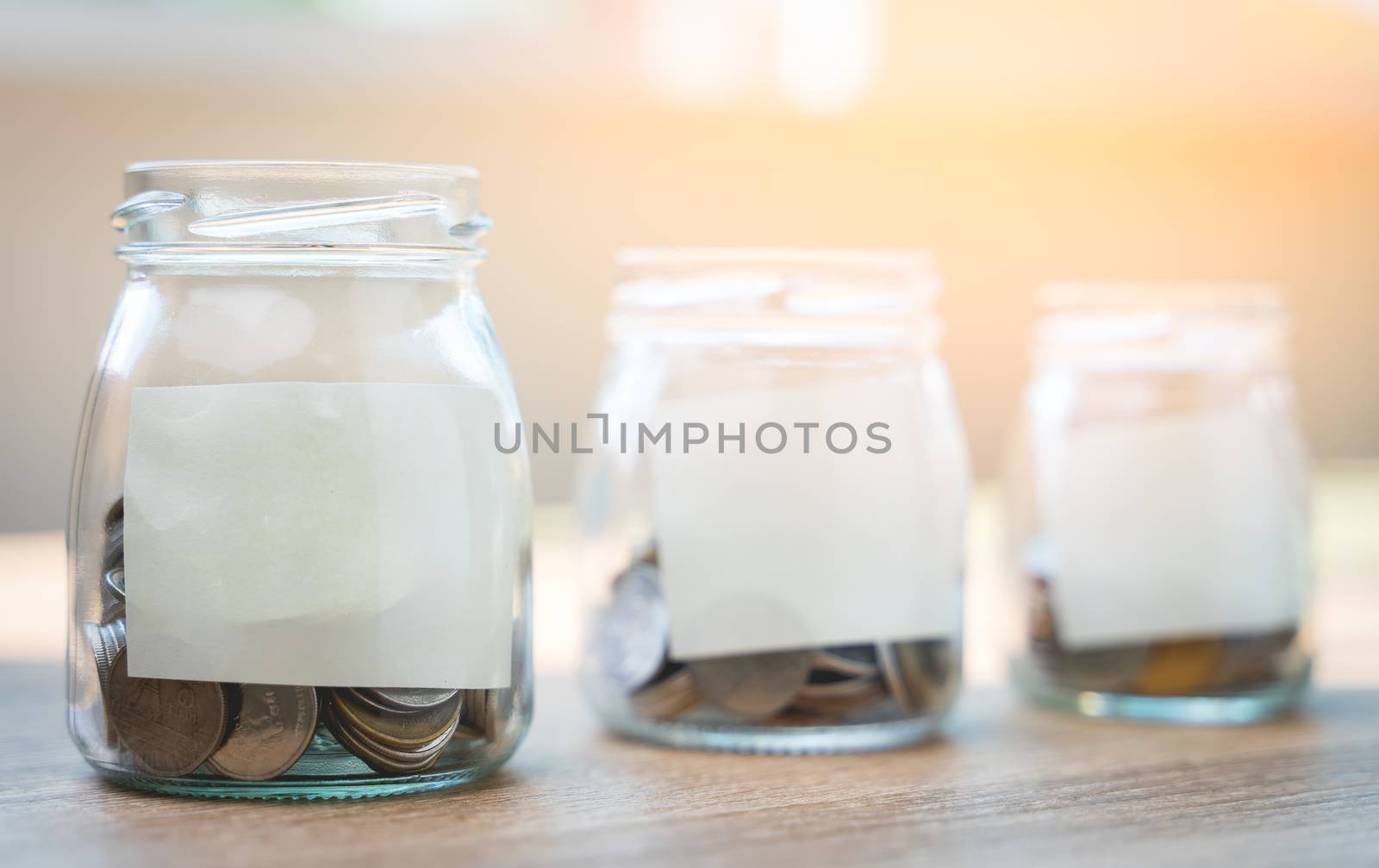 Money savings concepts. Put coins in glass bottles with paper label to spend on expenses such as savings, tourism, investment, emergency, retirement on wooden table with blur background