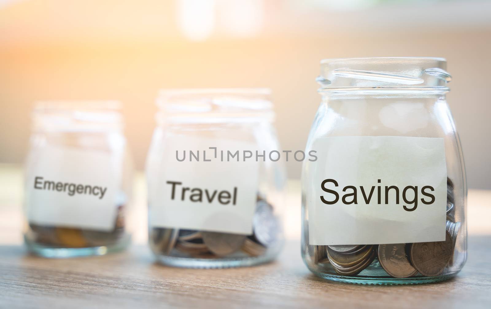 Money savings concepts. Put coins in glass bottles with paper label and text to spend on expenses such as savings, tourism, investment, emergency, retirement on wooden table with blur background