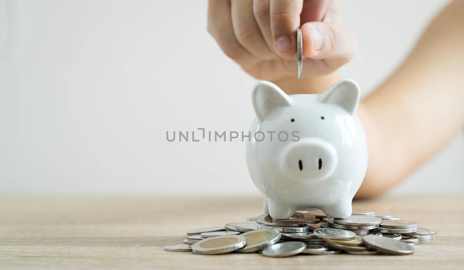 Money savings concepts hand holding coin to put in piggy bank to spend on expenses such as savings, tourism, investment, emergency, retirement on wooden table with blur background and copy space