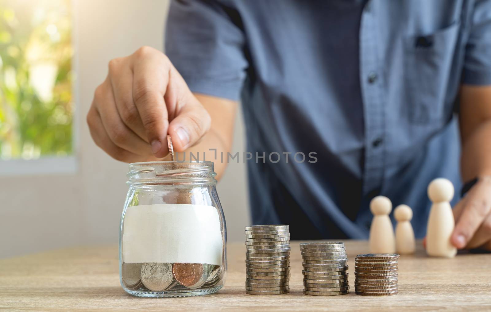 Money savings concepts  Glass bottle and stack coins with blur Men are coining in Glass bottel for saving money for families with family wooden dolls on wooden table with blur background, selective focus