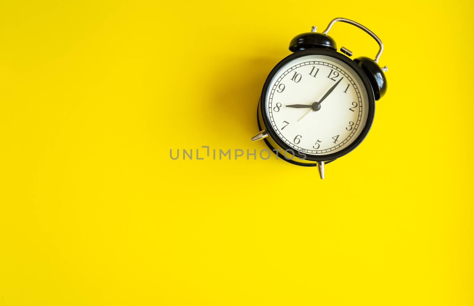 black alarm clock from 7 a.m. to 8 a.m. with bright yellow  background and shadows from the changing light of the sun's movements in morning and working hours concept front shot