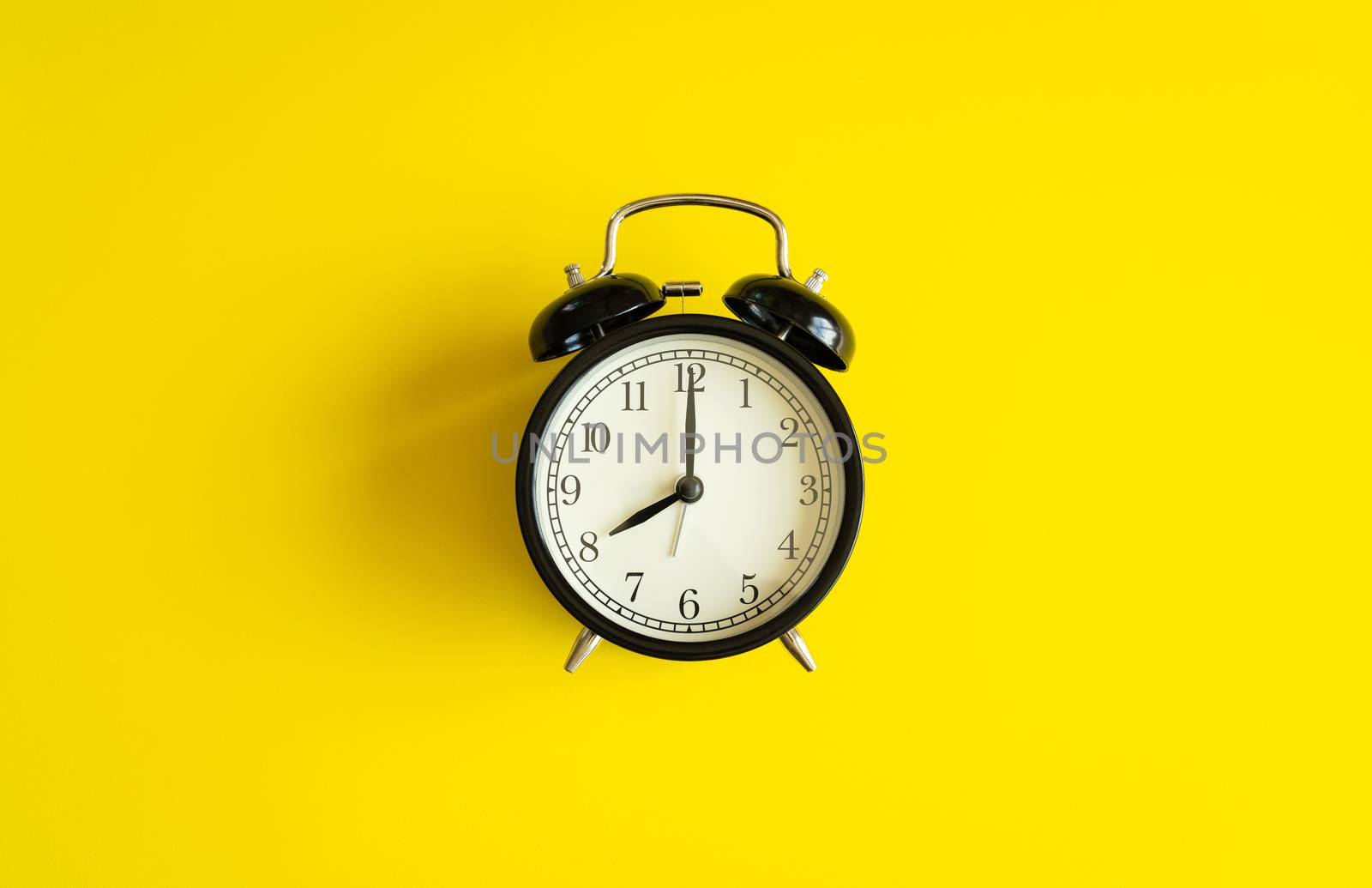 black alarm clock from 7 a.m. to 8 a.m. with bright yellow  background and shadows from the changing light of the sun's movements in morning and working hours concept front shot