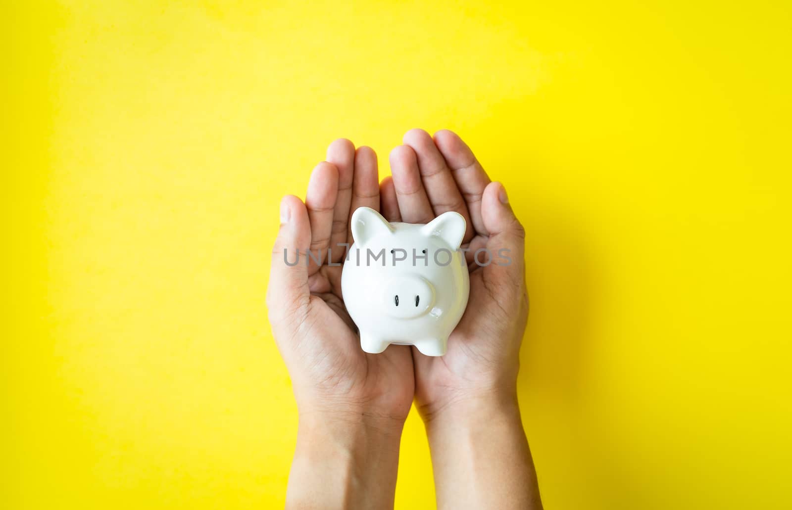 Money savings concepts. The piggy bank in hand is giving for savings, tourism, investment, emergency, retirement on yellow background and copy space