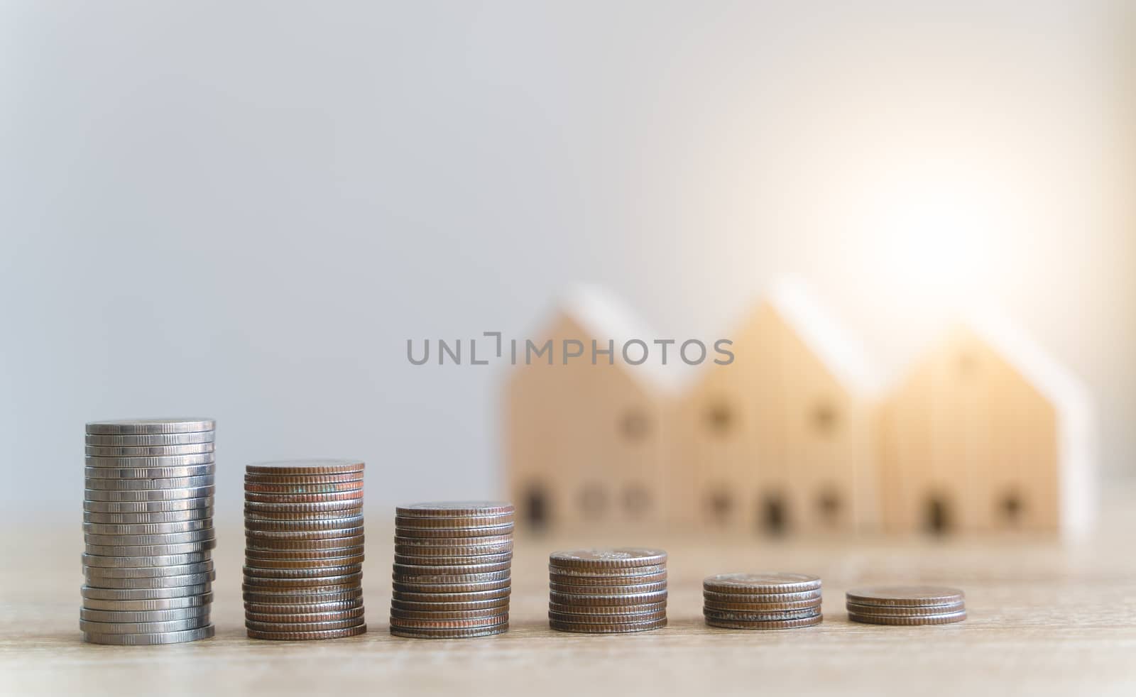 Money savings concepts. Stacked coins with blur wooden house in meaning about saving money to buy a house, refinancing, investment or financial on wooden table with blur background and copy space