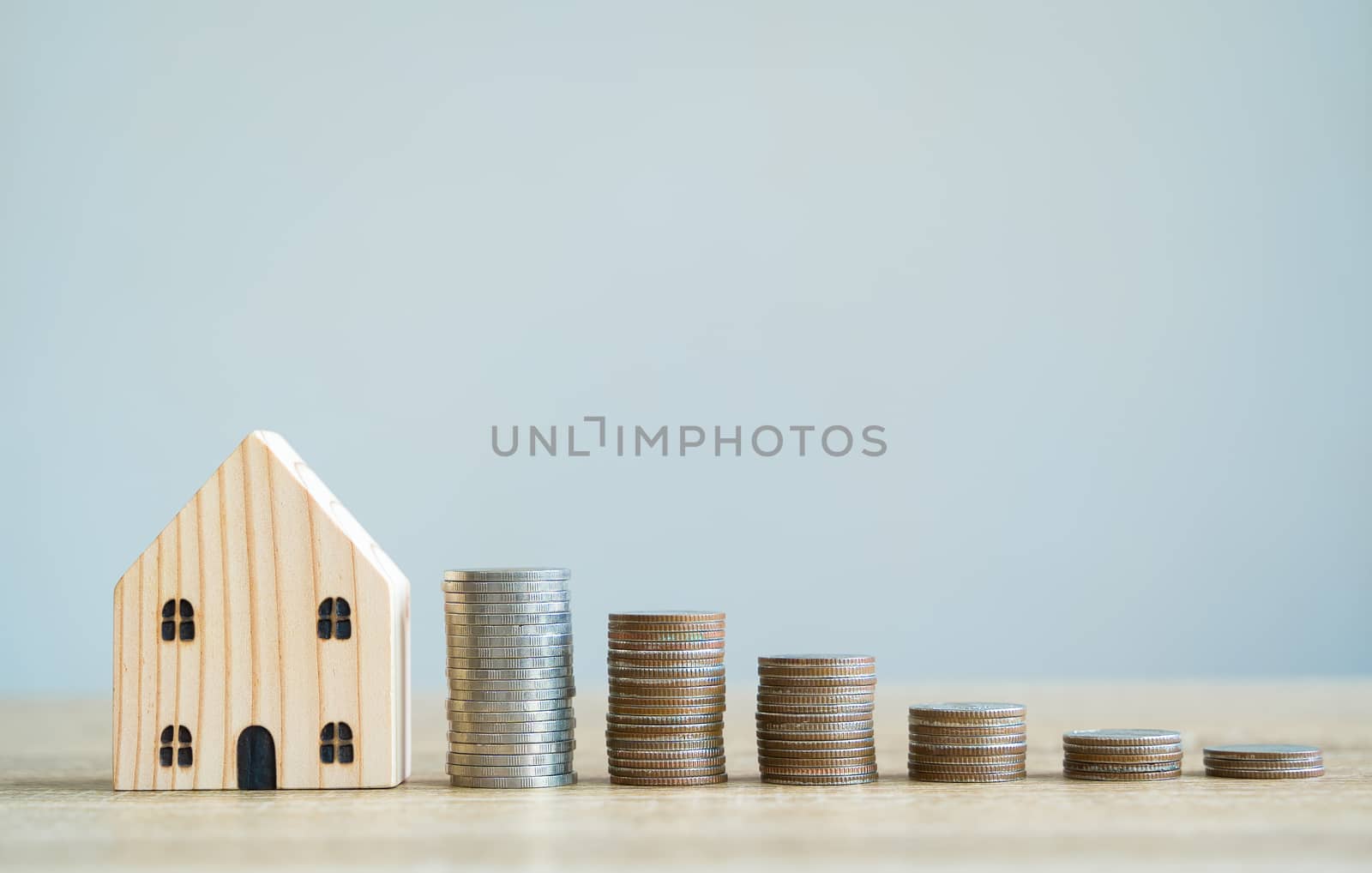Money savings concepts. Wooden house models with stacked coins in meaning about saving money to buy a house, refinancing, investment or financial on wooden table with blur background and copy space