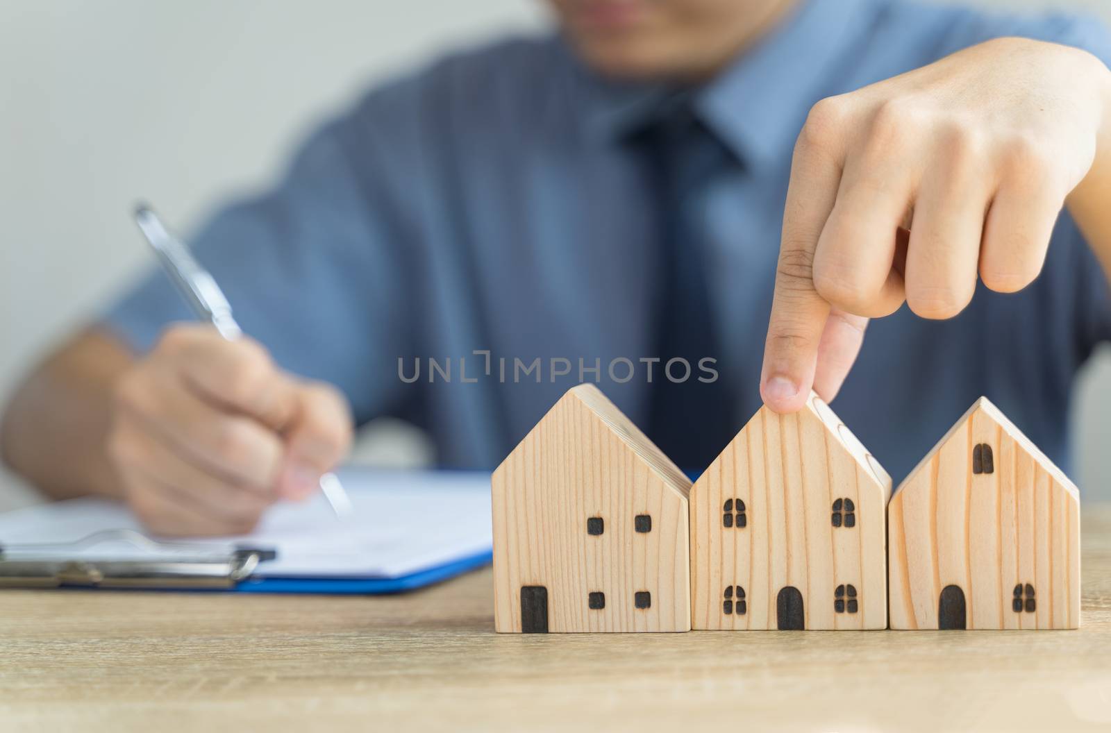 Hand pick House Wooden model in real estate , seller or buyer , loan concept with blur loan employee or realtor he's checking details about the sale of the house ,home Mortgage or home lone