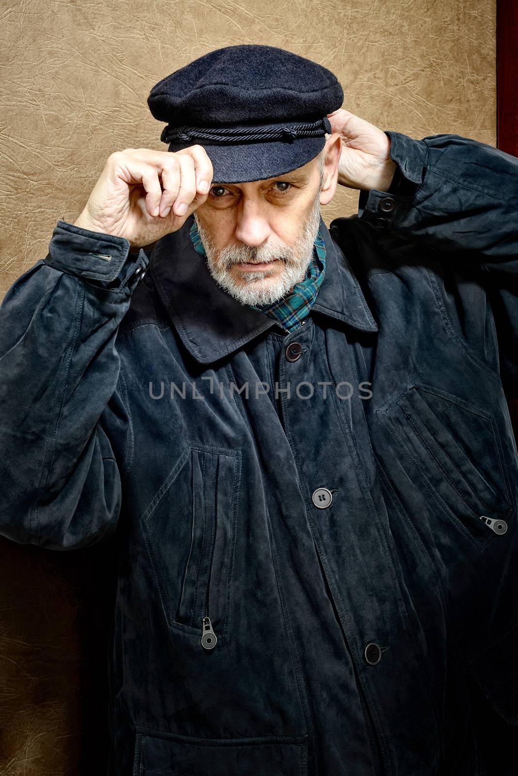 Portrait of a mature man with a white beard adjusting his cap on the head. He could be a sailor, a worker, a docker, or even a gangster or a thug. He has a penetrating gaze.