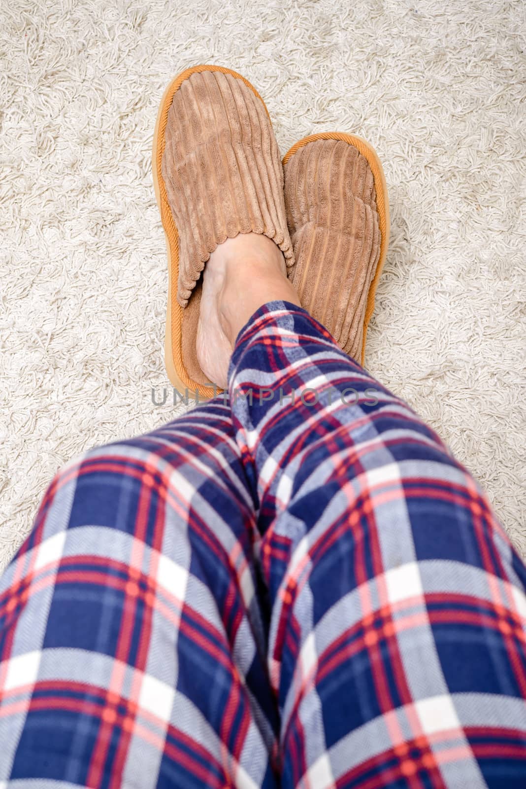 A man with hairy legs, wearing warm slippers and pajamas is relaxing with the feet on a wool carpet