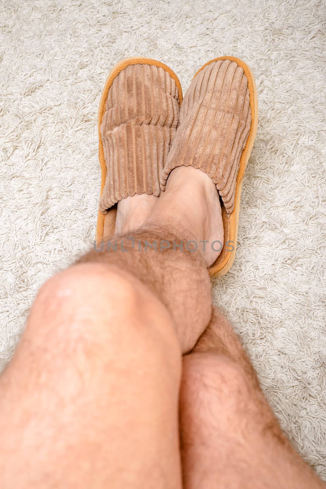 A man with hairy legs is wearing warm slippers and relaxing with the feet on a wool carpet